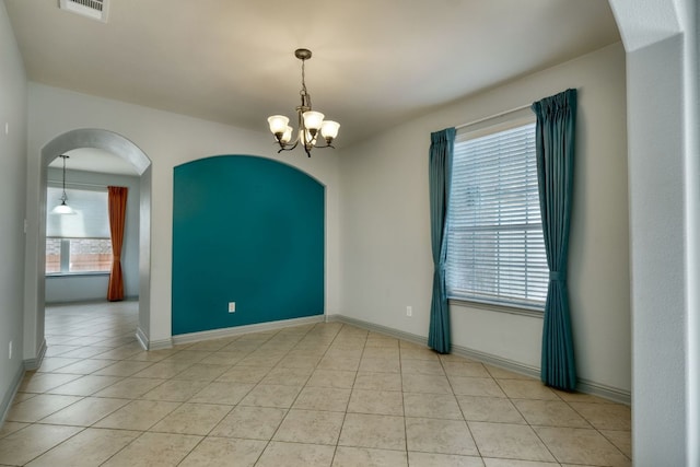 unfurnished room with a chandelier, arched walkways, light tile patterned flooring, and baseboards