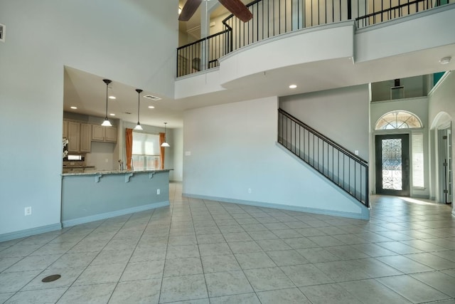 unfurnished living room featuring a high ceiling, light tile patterned floors, stairway, ceiling fan, and baseboards