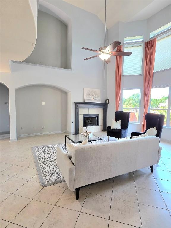 living area with high vaulted ceiling, a tiled fireplace, a ceiling fan, light tile patterned floors, and arched walkways
