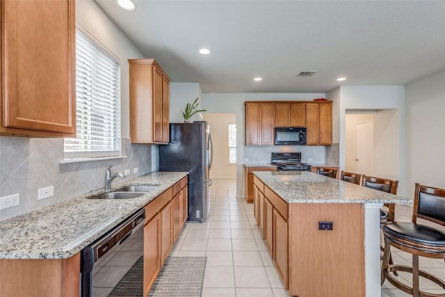 11905 Reindeer Dr, Austin, TX 78754 - kitchen featuring black appliances, a center island, a breakfast bar, tasteful backsplash, and light stone countertops