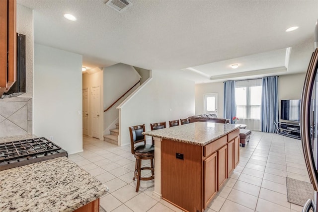 11905 Reindeer Dr, Austin, TX 78754 - kitchen with a kitchen bar, light tile patterned floors, brown cabinetry, light stone counters, and a center island
