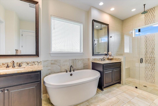 bathroom with a stall shower, a freestanding tub, two vanities, and recessed lighting