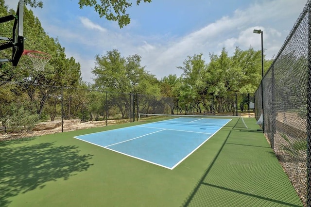 view of tennis court featuring fence and view of wooded area