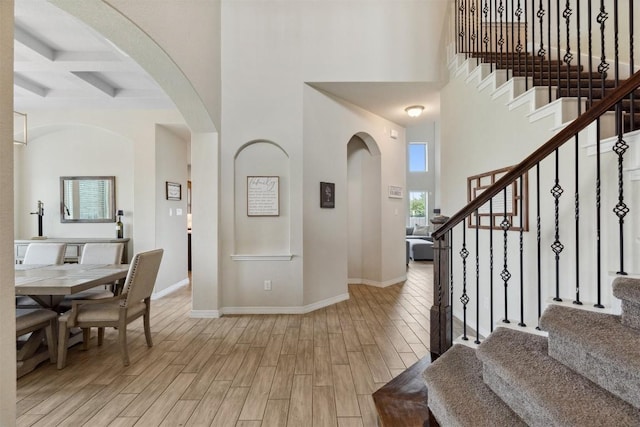 foyer entrance featuring wood finish floors, baseboards, stairway, beamed ceiling, and a high ceiling