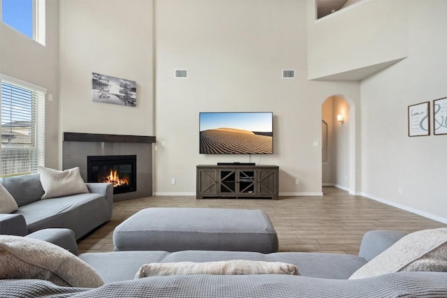 living area with a high ceiling, arched walkways, baseboards, a tile fireplace, and wood finished floors