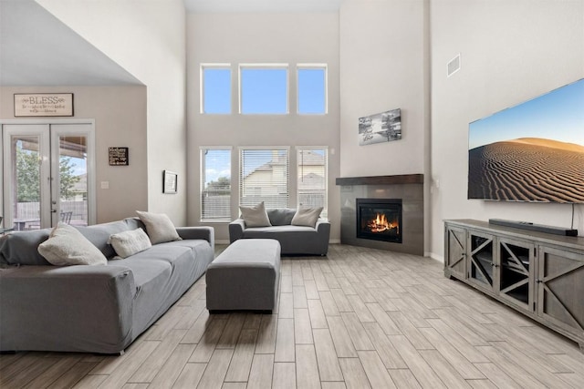 living area featuring a towering ceiling, french doors, wood finished floors, a tile fireplace, and baseboards