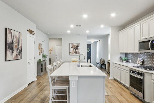 2024 Cantonata Dr, Leander, TX 78641 - kitchen with stainless steel appliances, backsplash, a kitchen island with sink, light countertops, and light wood finished floors