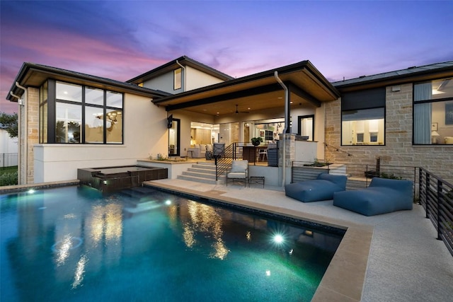 back of property at dusk with a patio, stone siding, stucco siding, and a pool with connected hot tub
