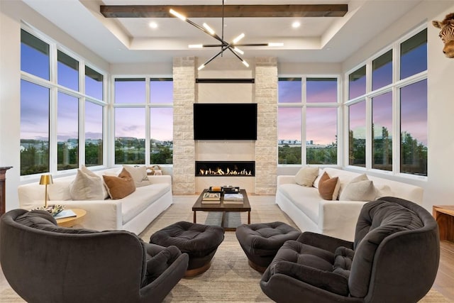 living area featuring wood finished floors, a stone fireplace, a towering ceiling, beamed ceiling, and a tray ceiling