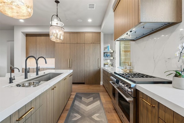 kitchen with double oven range, extractor fan, a sink, light wood finished floors, and light countertops