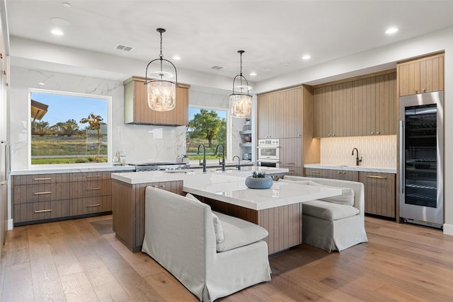 kitchen featuring beverage cooler, an island with sink, recessed lighting, decorative backsplash, and light wood-type flooring