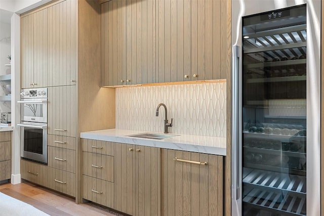 kitchen with a sink, wine cooler, light countertops, stainless steel double oven, and light wood-style flooring