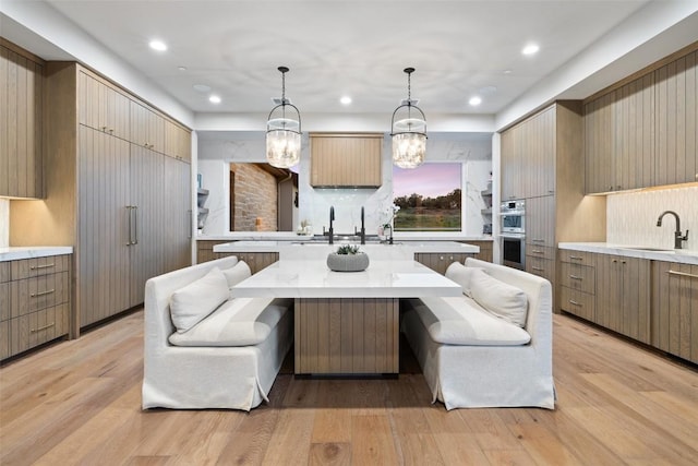 kitchen featuring a sink, backsplash, light countertops, light wood-type flooring, and recessed lighting