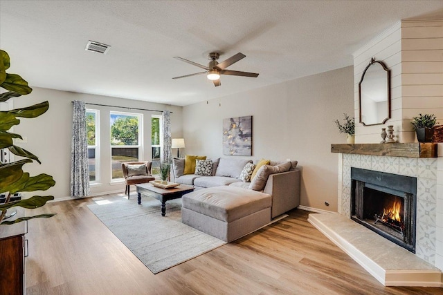 7605 Hawkeye Dr, Austin, TX 78749 - living room featuring a tile fireplace, a ceiling fan, light wood-type flooring, a textured ceiling, and baseboards
