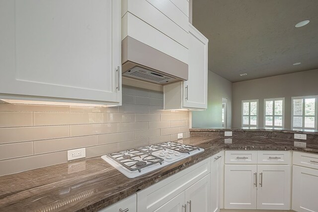 13403 Lakemeade Ct, Sugar Land, TX 77498 - kitchen featuring white gas stovetop, white cabinets, custom exhaust hood, backsplash, and dark stone countertops