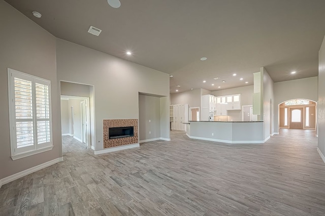 13403 Lakemeade Ct, Sugar Land, TX 77498 - unfurnished living room with light wood-style flooring, baseboards, recessed lighting, a tile fireplace, and a towering ceiling