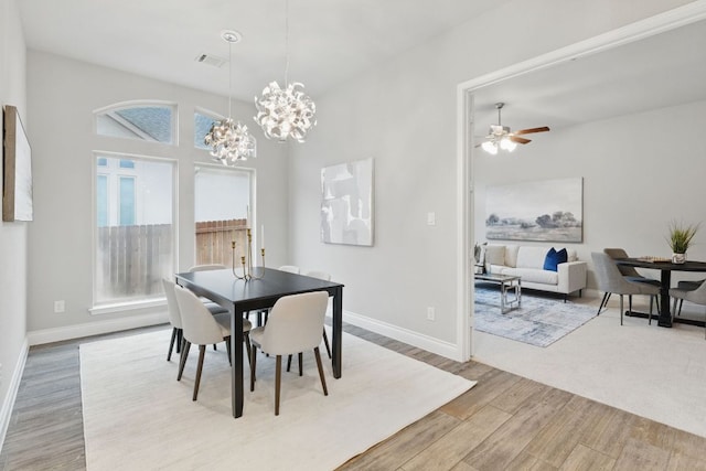 dining area featuring light wood-style flooring, a chandelier, ceiling fan, and baseboards
