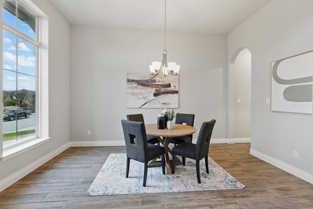 dining room with a chandelier, arched walkways, healthy amount of natural light, and wood finished floors