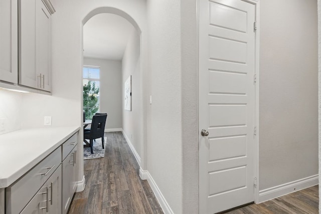corridor featuring arched walkways, dark wood finished floors, and baseboards