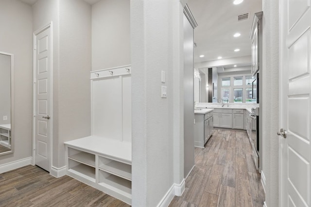 mudroom with wood finished floors, recessed lighting, baseboards, and a sink