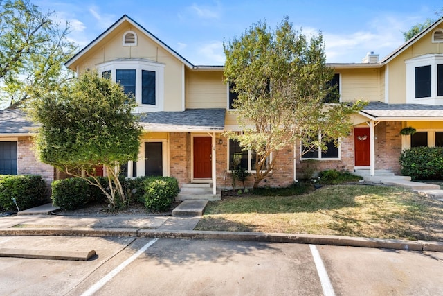 traditional home featuring uncovered parking, brick siding, a front lawn, and roof with shingles