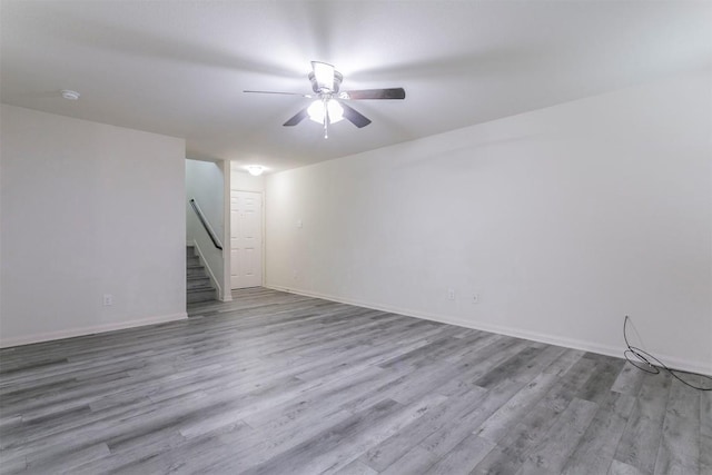 unfurnished living room with a ceiling fan, stairs, wood finished floors, and baseboards