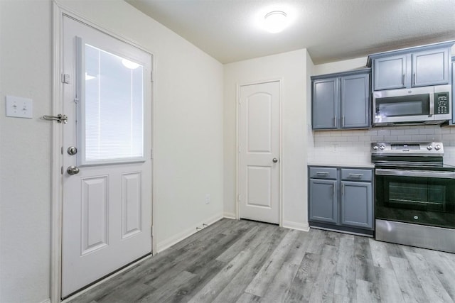 kitchen with stainless steel appliances, light wood-type flooring, decorative backsplash, gray cabinets, and baseboards