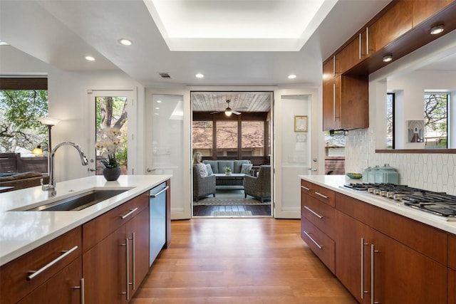 kitchen with appliances with stainless steel finishes, a sink, light countertops, backsplash, and light wood-style flooring