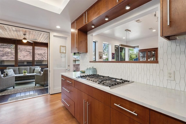 kitchen with stainless steel gas stovetop, decorative backsplash, light countertops, light wood-type flooring, and recessed lighting