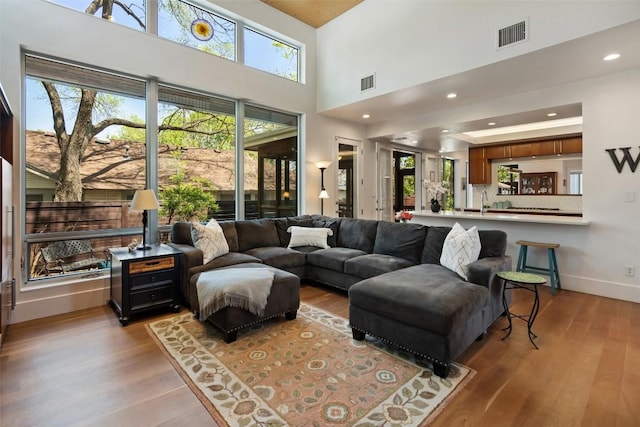 living room featuring wood finished floors, baseboards, recessed lighting, and a high ceiling