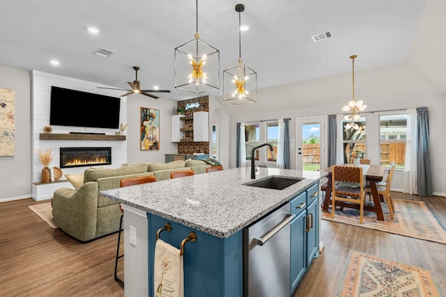 115 Oleander Loop, Buda, TX 78610 - kitchen with blue cabinets, stainless steel dishwasher, a large fireplace, vaulted ceiling, and wood finished floors