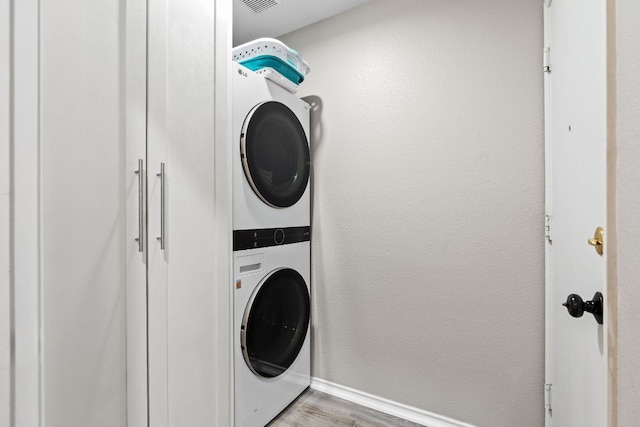 washroom with estacked washer and dryer, light wood finished floors, and baseboards
