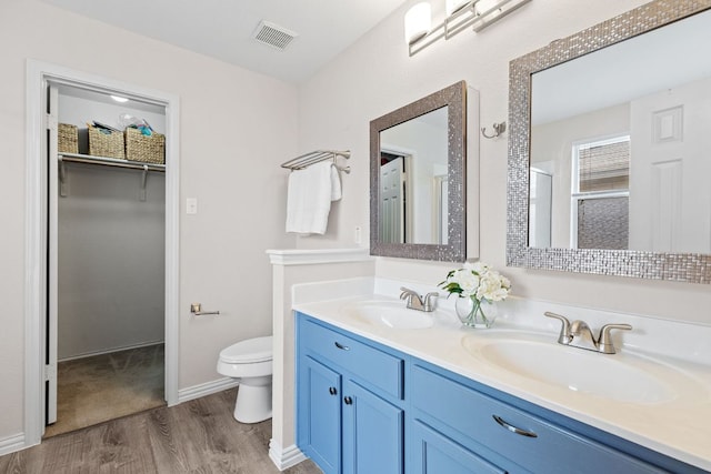 full bathroom featuring wood finished floors, toilet, double vanity, a shower with shower door, and a spacious closet