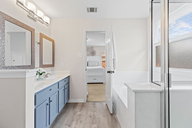 full bathroom with ensuite bath, wood finished floors, a bath, and double vanity