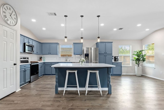 kitchen featuring appliances with stainless steel finishes, vaulted ceiling, blue cabinetry, decorative backsplash, and a center island