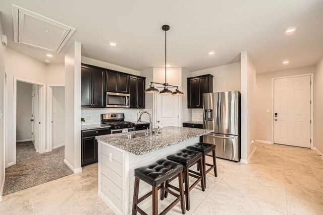 kitchen featuring appliances with stainless steel finishes, a sink, tasteful backsplash, light stone counters, and a center island with sink
