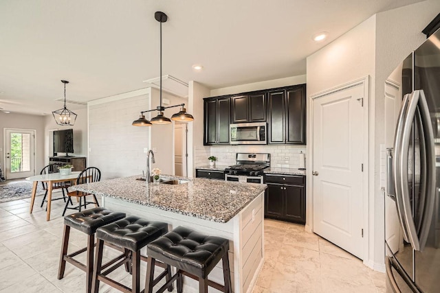 kitchen featuring stainless steel appliances, a sink, backsplash, stone counters, and a kitchen island with sink