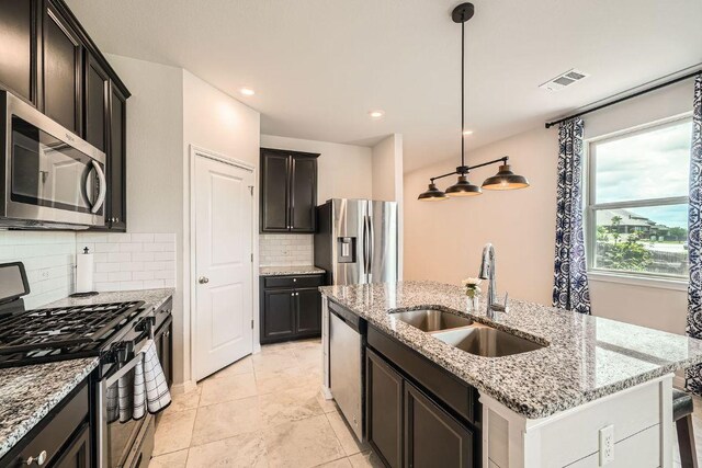 kitchen with appliances with stainless steel finishes, a sink, a center island with sink, decorative backsplash, and light stone counters