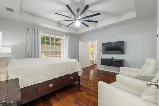 bedroom with a tray ceiling, hardwood / wood-style flooring, baseboards, and a ceiling fan