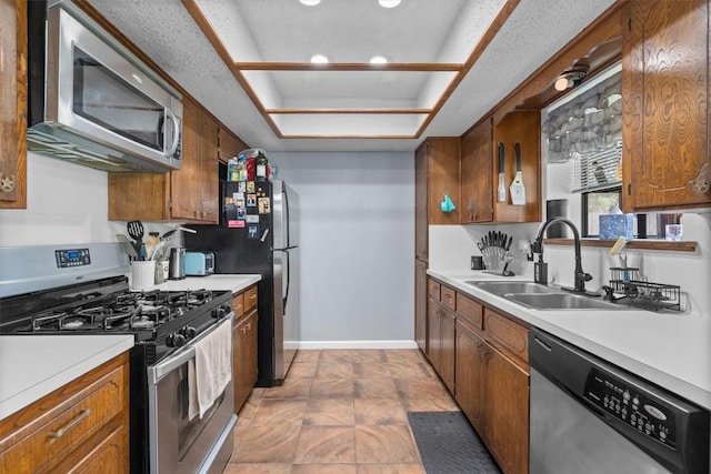 kitchen with stainless steel appliances, a sink, brown cabinetry, light countertops, and recessed lighting