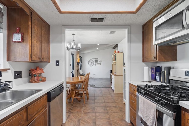 kitchen with appliances with stainless steel finishes, light countertops, a chandelier, brown cabinets, and a textured ceiling