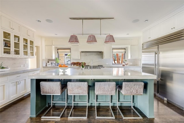 kitchen featuring stainless steel built in refrigerator, decorative backsplash, white cabinetry, and a kitchen bar