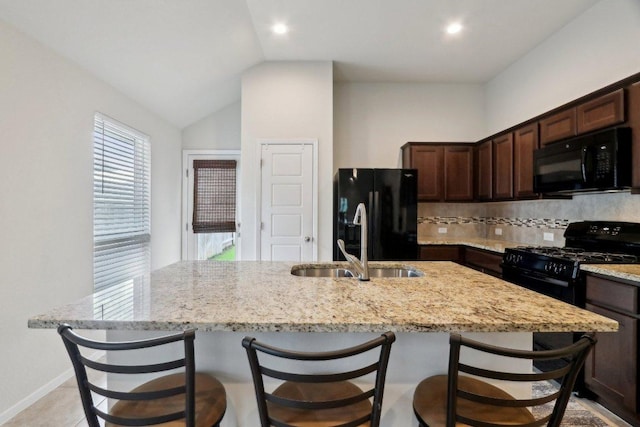 6032 Urbano Bnd, Round Rock, TX 78665 - kitchen featuring black appliances, a center island with sink, dark brown cabinets, light stone counters, and vaulted ceiling