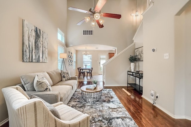 living area featuring a chandelier, wood finished floors, arched walkways, a towering ceiling, and a ceiling fan