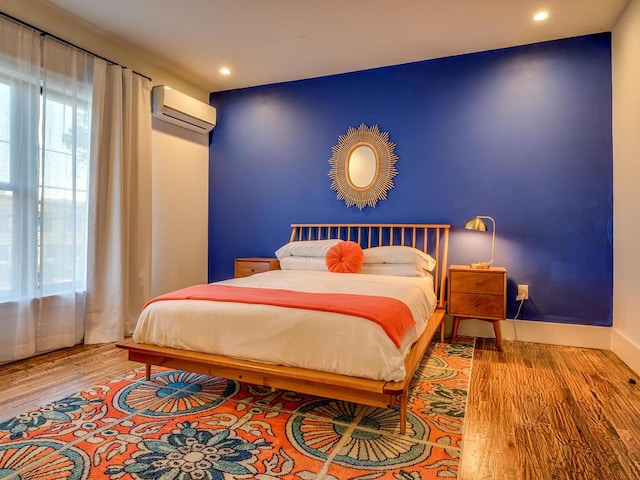 bedroom featuring an AC wall unit, wood finished floors, multiple windows, and recessed lighting