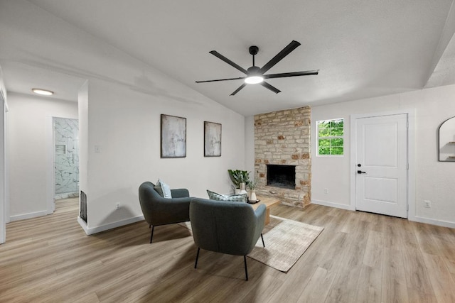 living room with ceiling fan, light wood-style floors, vaulted ceiling, baseboards, and a stone fireplace