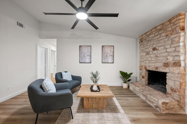 living room featuring lofted ceiling, ceiling fan, wood finished floors, a stone fireplace, and baseboards