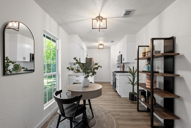 dining room with light wood-style flooring, baseboards, and a textured ceiling
