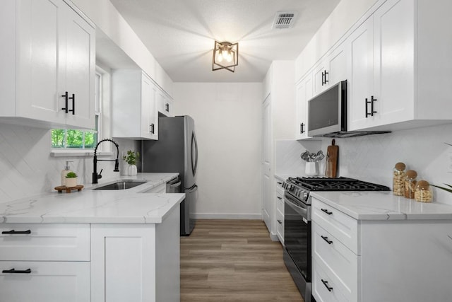 7002 Teaberry Dr, Austin, TX 78745 - kitchen featuring appliances with stainless steel finishes, backsplash, light wood-style flooring, white cabinetry, and light stone countertops