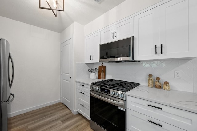 kitchen with appliances with stainless steel finishes, decorative backsplash, light wood-style floors, light stone countertops, and white cabinetry